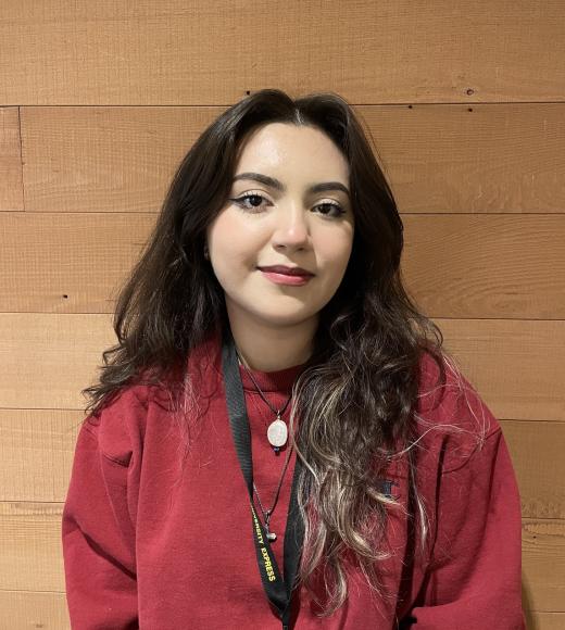 Lupe standing in front of wood paneling wearing a red sweatshirt and rocking cat eyes
