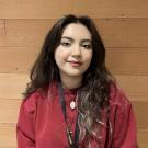 Lupe standing in front of wood paneling wearing a red sweatshirt and rocking cat eyes